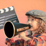 Kid holding clapper board against summer sky background. Cinema concept